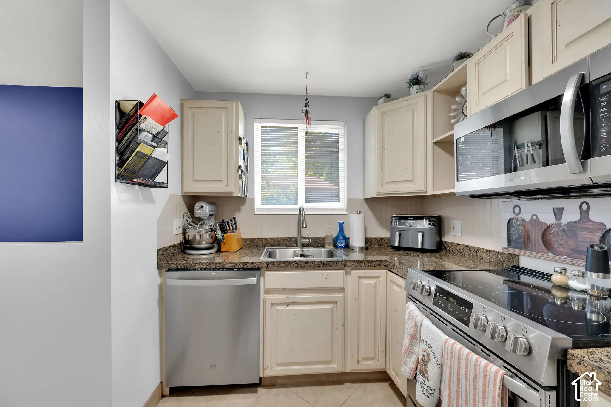 Kitchen featuring light-toned cabinetry, a stainless steel dishwasher, a stainless steel range with a smooth cooktop, a stainless steel microwave, and granite countertops