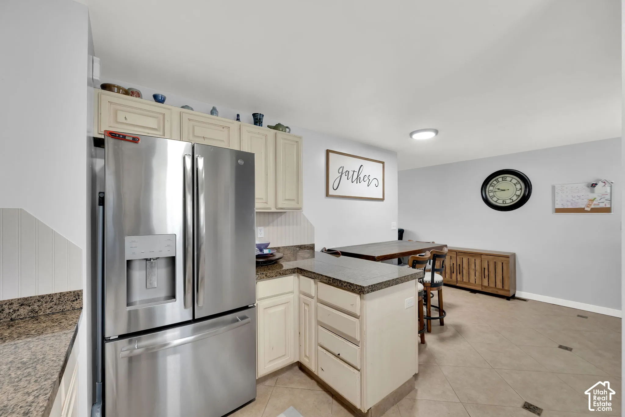 Stainless steel refrigerator, light-toned cabinetry, speckled countertops, tile flooring, and a recessed ceiling light