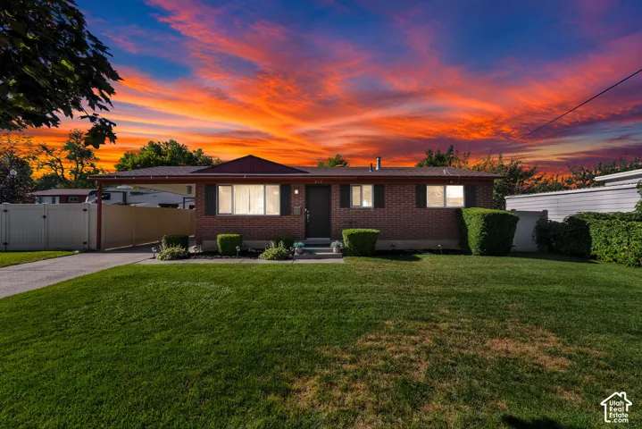 Brick exterior with a carport, front lawn, mature landscaping, and an asphalt driveway