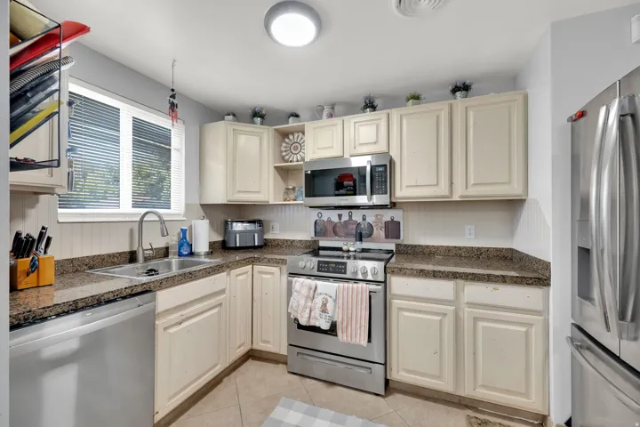 Kitchen featuring light-toned cabinetry, stainless steel appliances, granite-look countertops, a stainless steel sink, and a window with blinds