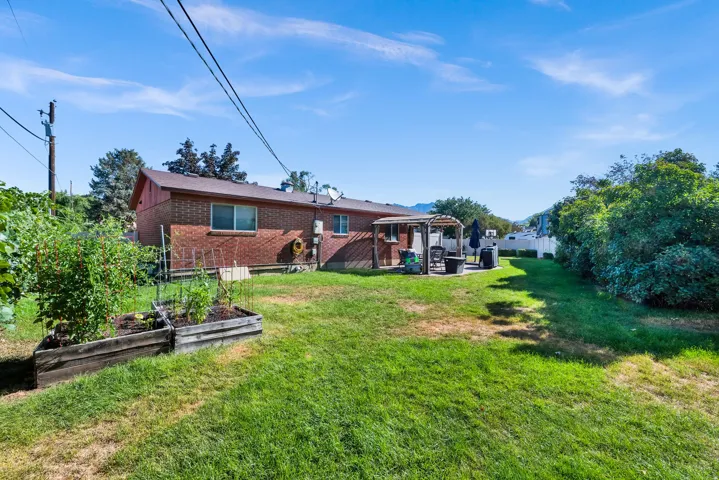Expansive backyard featuring a brick exterior, a paved patio with a pergola, raised garden beds, and mature perimeter landscaping