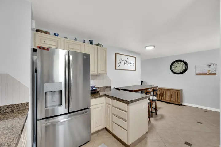 Stainless steel refrigerator, light-toned cabinetry, speckled countertops, tile flooring, and a recessed ceiling light