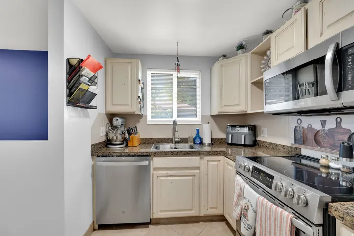 Kitchen featuring light-toned cabinetry, a stainless steel dishwasher, a stainless steel range with a smooth cooktop, a stainless steel microwave, and granite countertops
