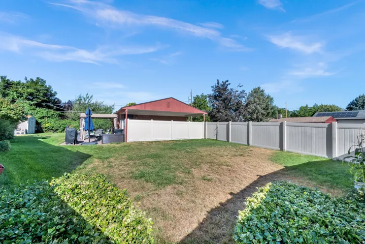 Expansive backyard featuring a privacy fence, covered patio, and mature landscaping