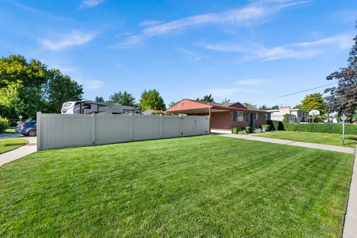 Expansive front yard with a manicured lawn, concrete walkway, and privacy fencing