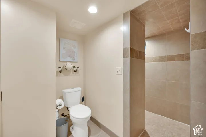 Recessed ceiling lighting, tiled shower walls, tiled shower floor, and a white toilet
