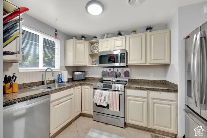 Kitchen featuring light-toned cabinetry, stainless steel appliances, granite-look countertops, a stainless steel sink, and a window with blinds