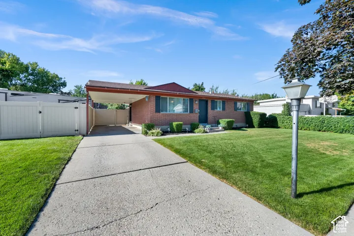 Brick exterior with a covered carport, concrete driveway, and a fenced side yard