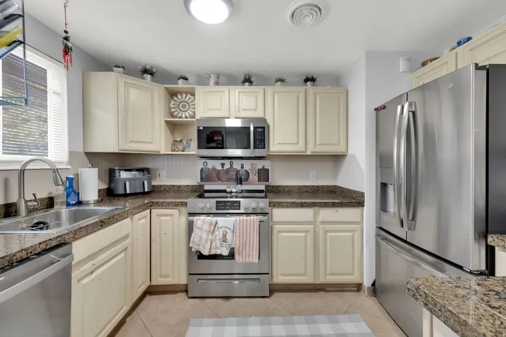 Kitchen featuring stainless steel appliances, neutral cabinetry, patterned countertops, and tile flooring