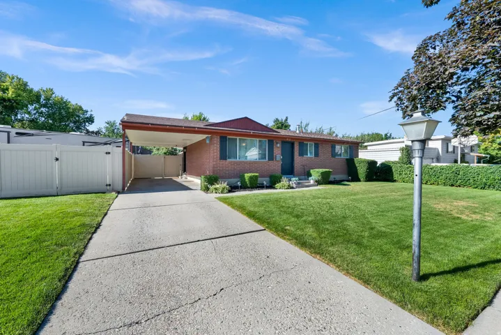 Brick exterior with a covered carport, concrete driveway, and a fenced side yard