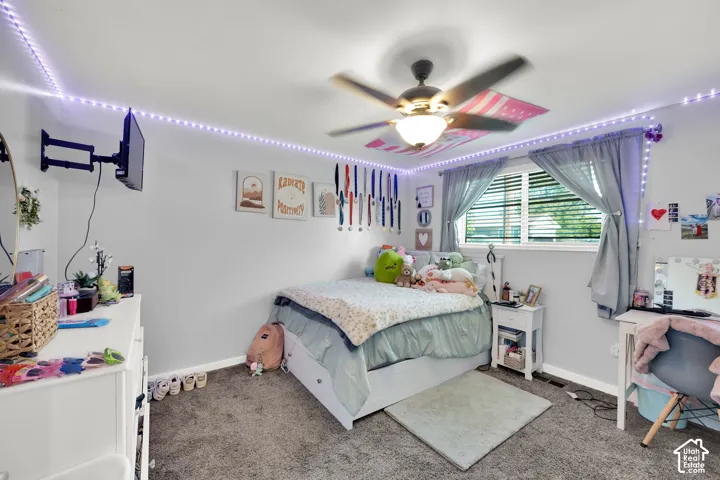Wall-mounted television bracket, ceiling fan with integrated lighting, window with blinds and gray curtains, gray wall paint, and gray carpet flooring