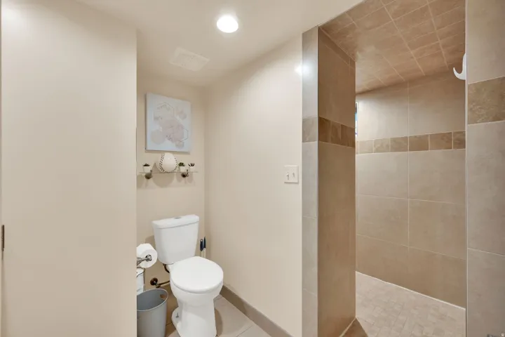 Recessed ceiling lighting, tiled shower walls, tiled shower floor, and a white toilet