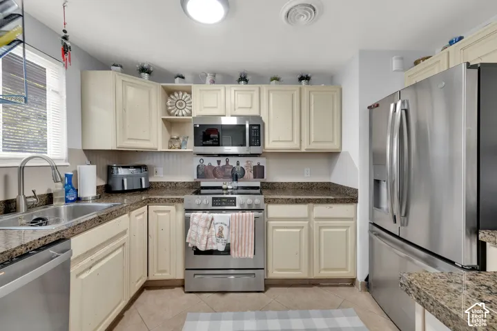 Kitchen featuring stainless steel appliances, neutral cabinetry, patterned countertops, and tile flooring