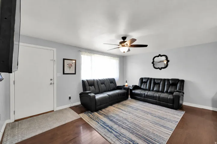 Hardwood flooring, light gray wall paint, large window, ceiling fan with light fixture, and white trim