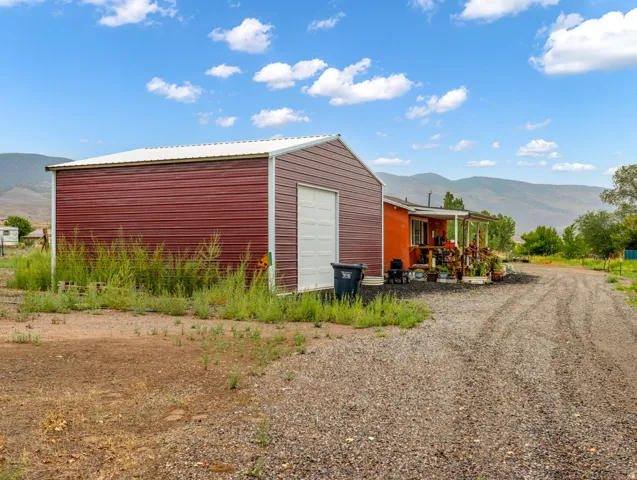 Detached metal building with a white overhead door, gravel driveway, and a covered porch
