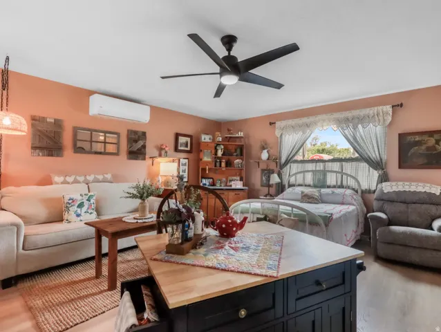 Wood-finish flooring throughout, featuring a ceiling fan with integrated lighting, built-in shelving, and a wall-mounted air conditioning unit