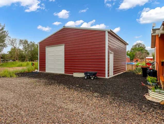 Red metal building featuring a white roll-up garage door, a white side entry door, and a gravel foreground
