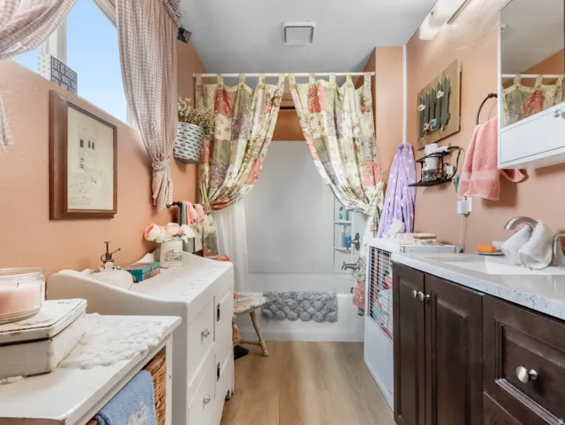 Bathroom featuring a built-in bathtub, a window, wood-finish flooring, and a vanity with a white countertop