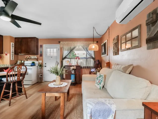 Wood-finish flooring, dark wood cabinetry, a ceiling fan with integrated lighting, a wall-mounted AC unit, and a white paneled door
