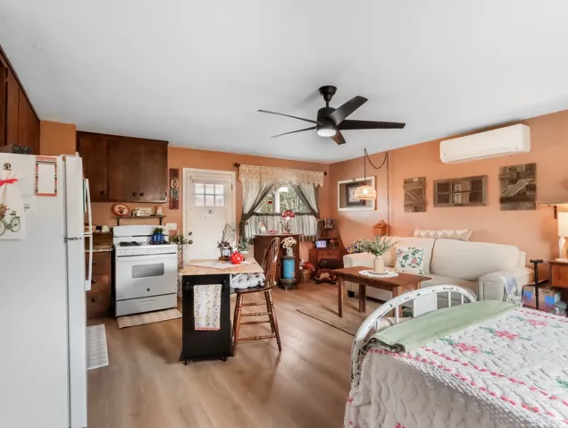Wood-finish flooring, dark wood cabinetry, white kitchen appliances, wall-mounted air conditioning unit, and a ceiling fan