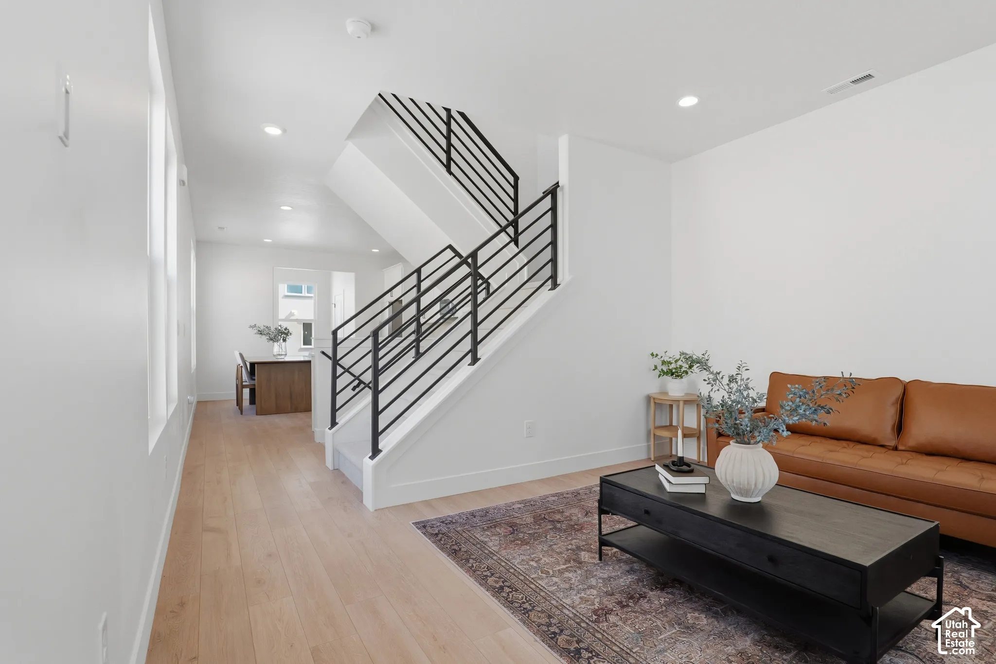 Light wood-finish flooring throughout, modern black metal stair railings, recessed lighting, and white wall finishes