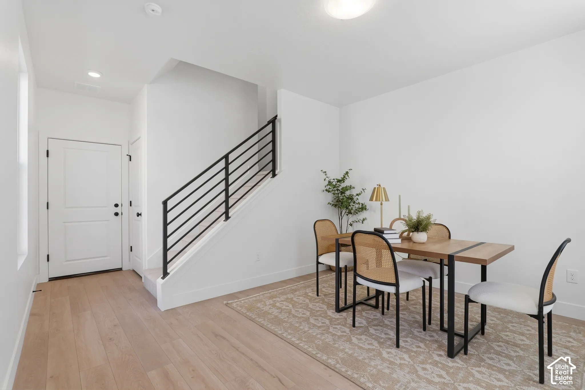 Light wood-finish flooring, white walls, white paneled door, and a staircase with black horizontal railings