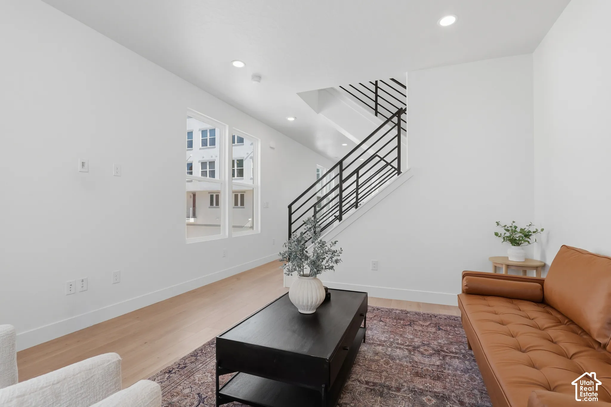 Light wood-finish flooring, recessed ceiling lighting, a modern black metal staircase railing, and white walls