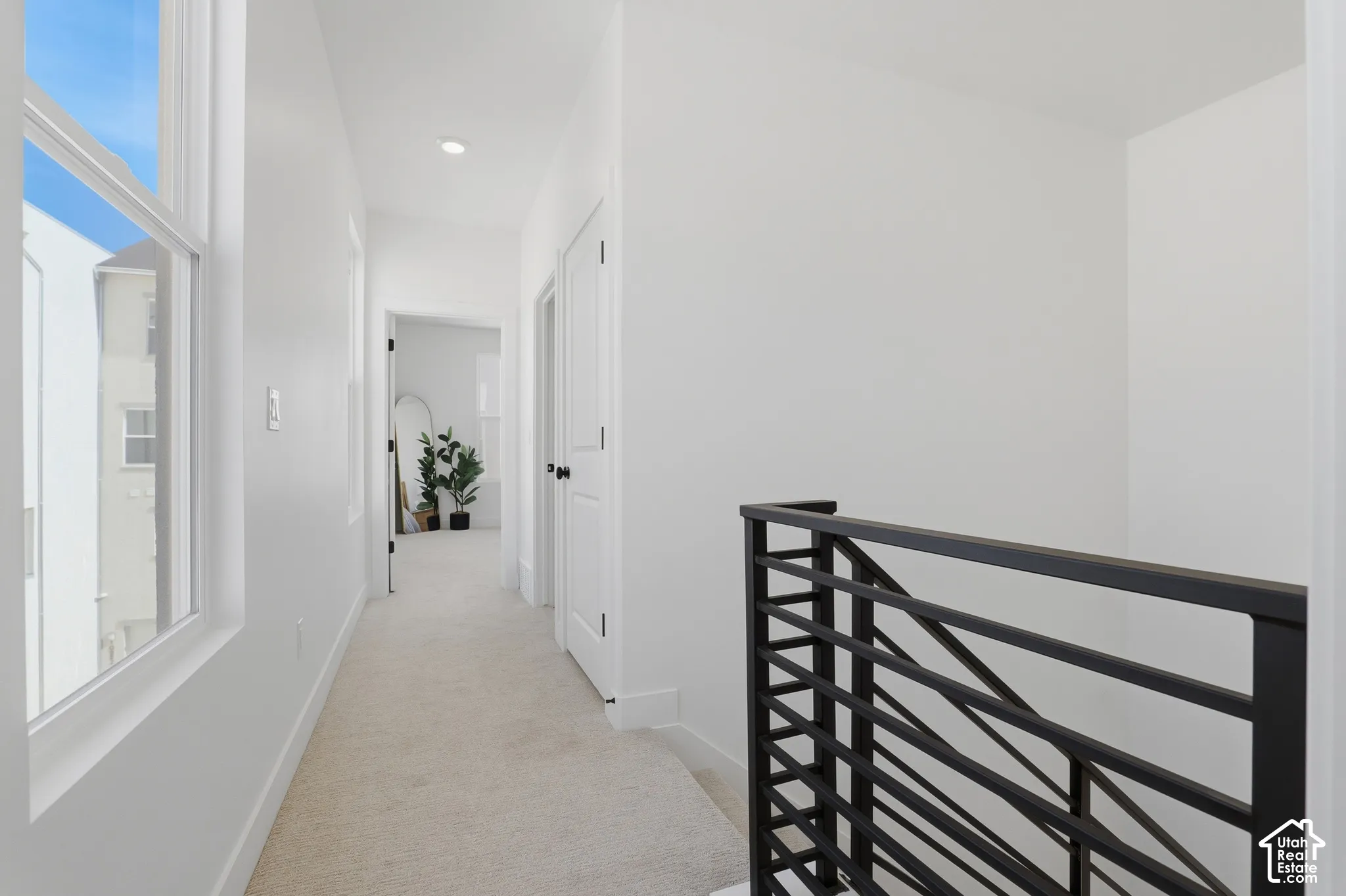 Hallway featuring neutral carpet flooring, recessed lighting, and a modern black metal railing