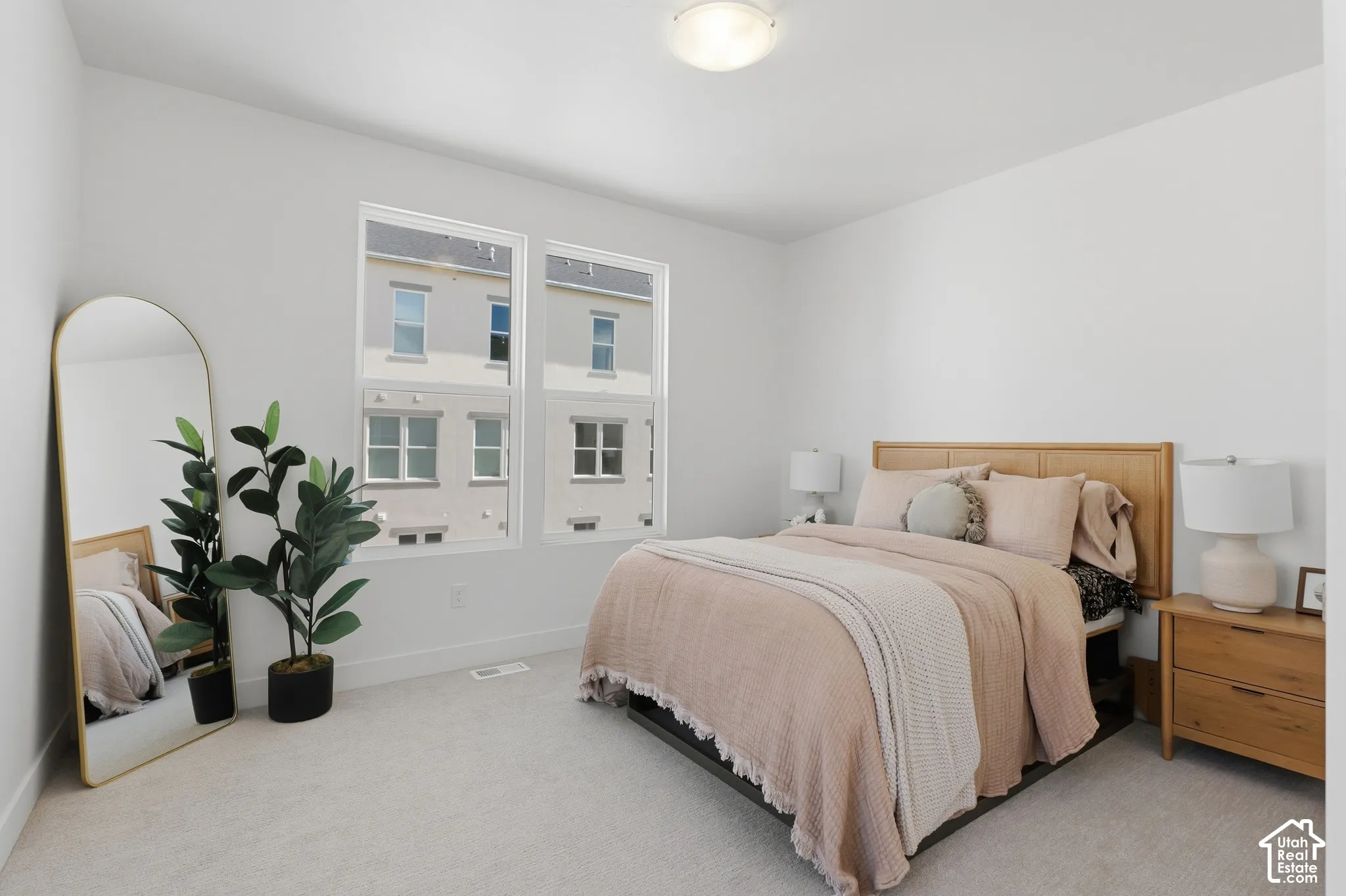 Two large windows providing abundant natural light, light-toned carpet flooring, recessed ceiling light fixture, and a light wood-finish headboard