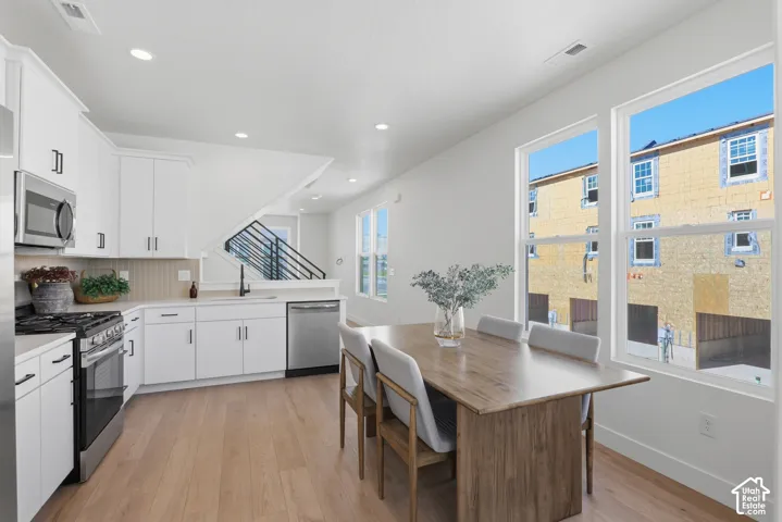 Open-concept kitchen with white cabinetry, light countertops, wood-finish flooring, and stainless steel appliances