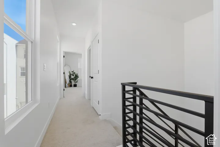 Hallway featuring neutral carpet flooring, recessed lighting, and a modern black metal railing