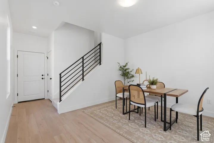 Light wood-finish flooring, white walls, white paneled door, and a staircase with black horizontal railings