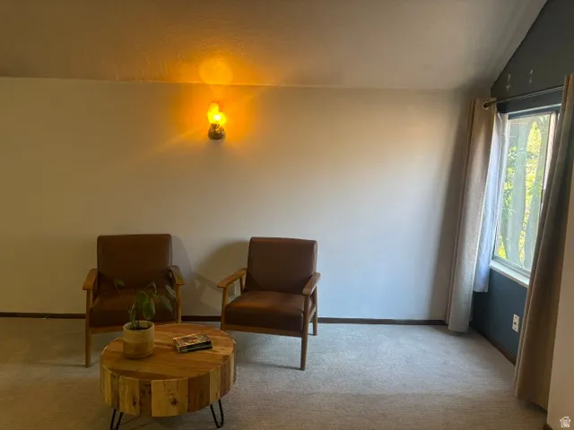 Carpeted flooring with a window featuring drapes and a wall-mounted light fixture