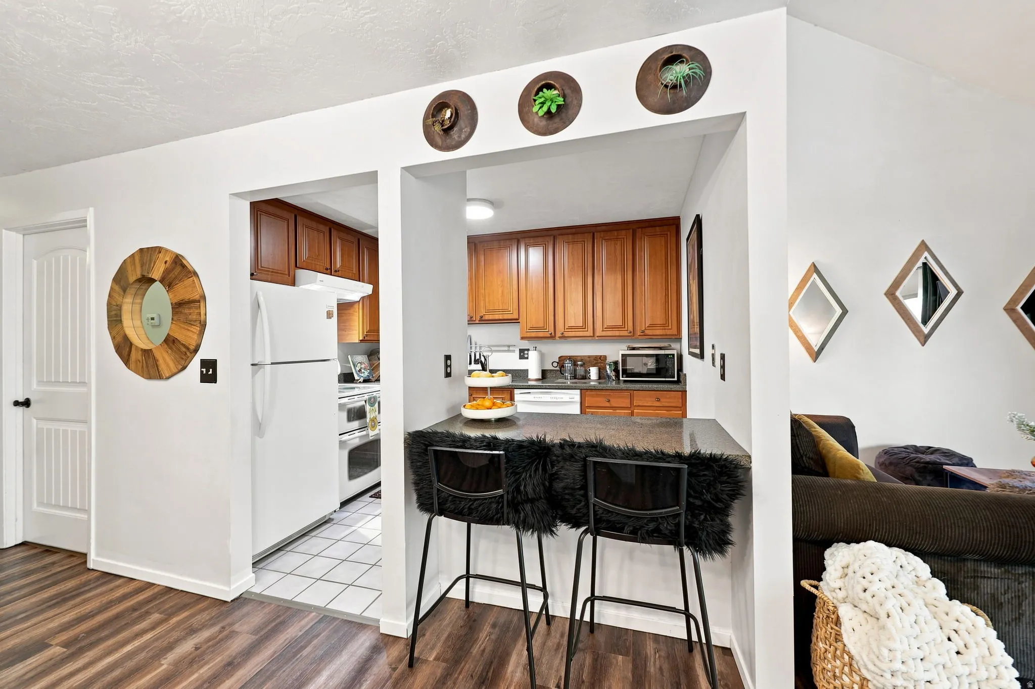 Wood-finish flooring, white paneled door, kitchen pass-through with counter, wood cabinetry, and white appliances