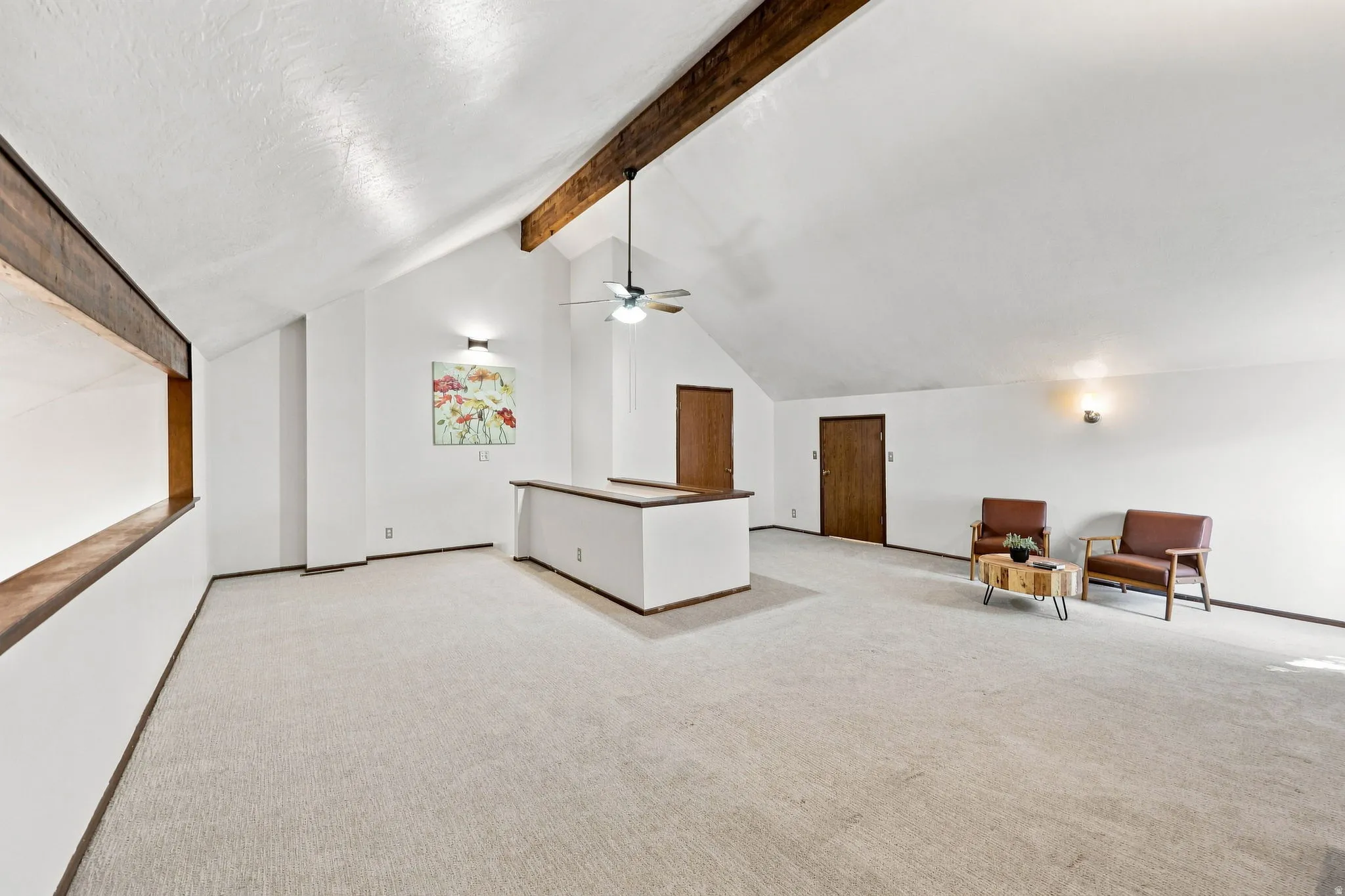 Vaulted ceiling with exposed wood beams, ceiling fan, carpet flooring, and two wood-finish doors