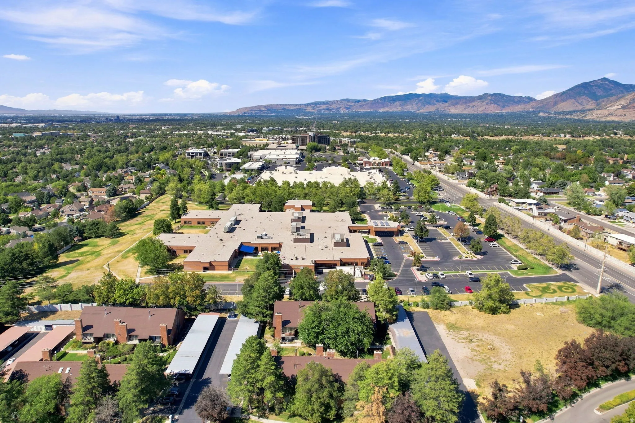 Expansive property featuring a large building with multiple wings, abundant surface parking, and surrounding mature trees