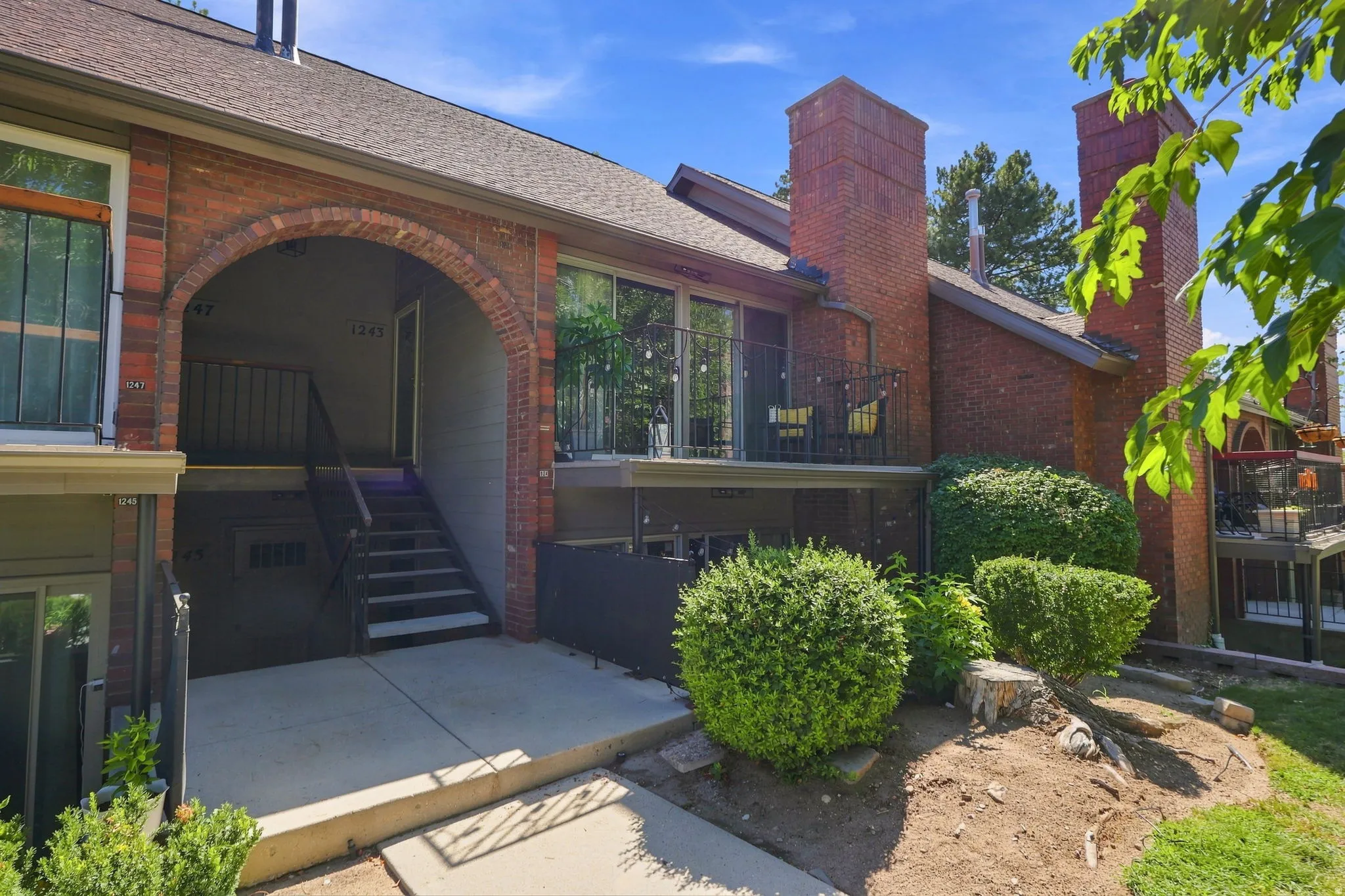 Brick exterior with a prominent arched entrance, multiple balconies with dark railings, brick chimneys, and an asphalt shingle roof