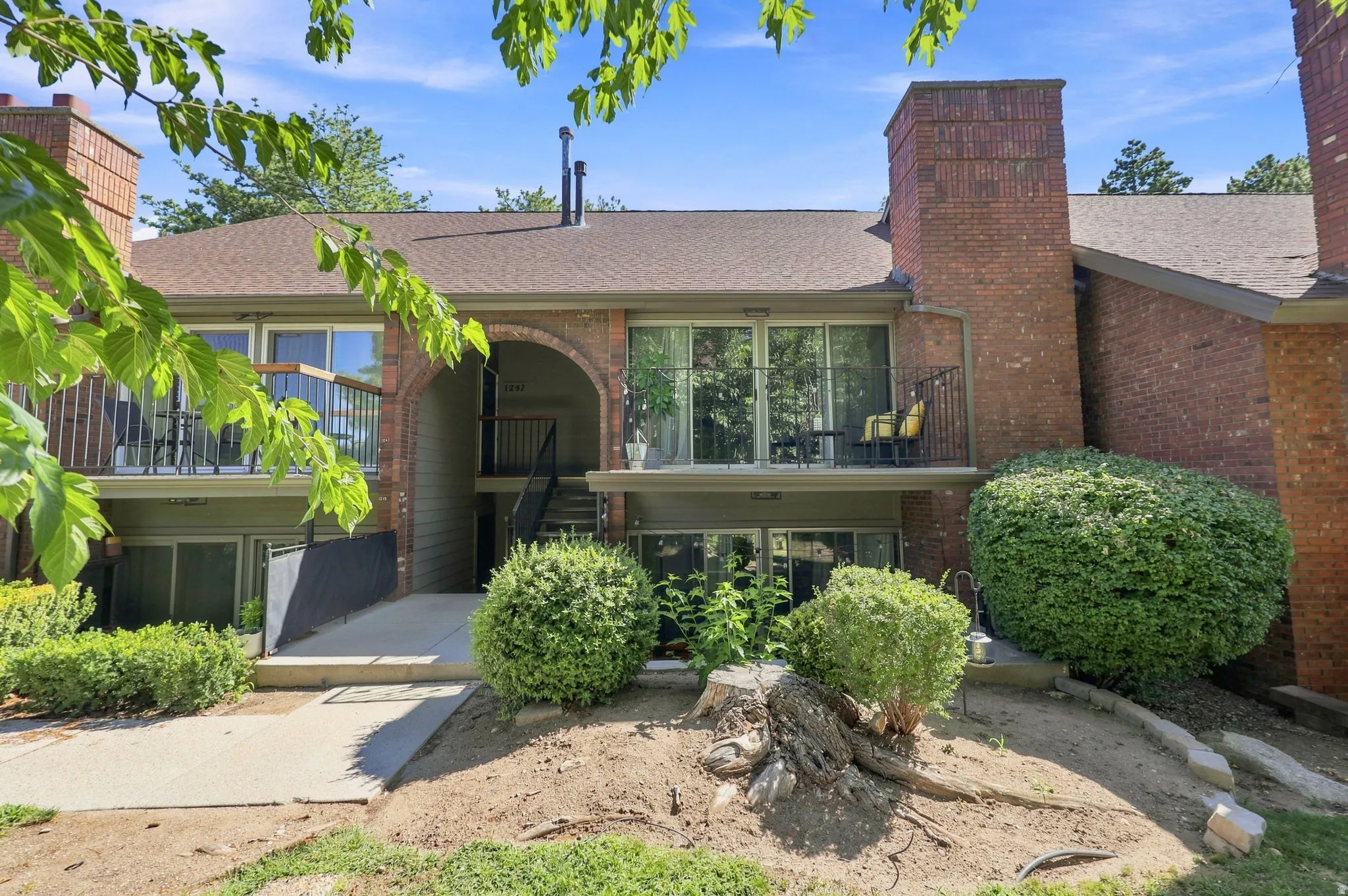 Brick exterior with multiple balconies, a sloped shingle roof, and established landscaping