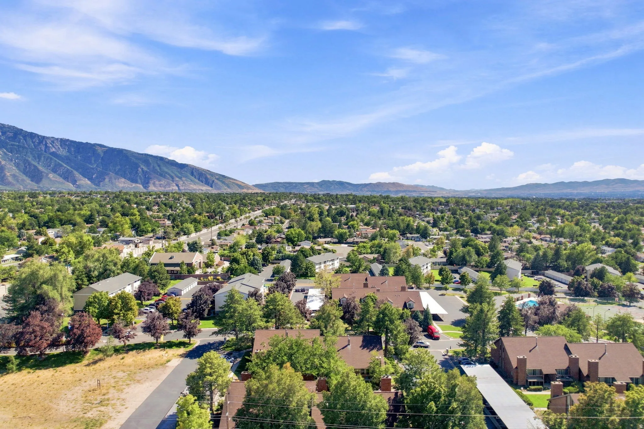 Expansive residential area with a prominent mountain backdrop, featuring a dense tree canopy, varied housing structures, and a clear blue sky