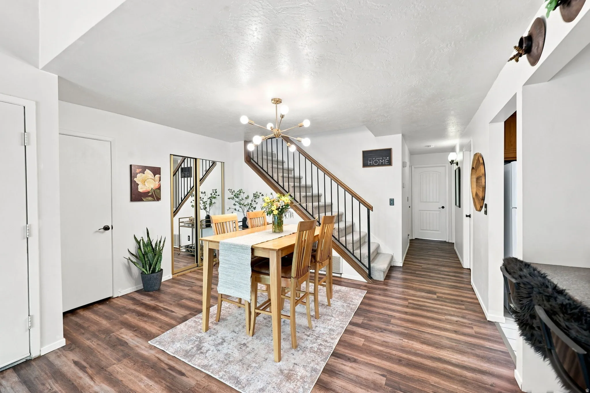Wood-finish flooring throughout, modern sputnik chandelier, and a carpeted staircase with a dark metal and wood railing