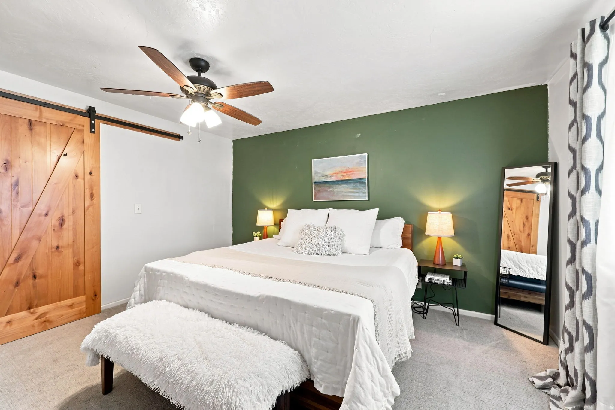 Wood barn door with black track hardware, ceiling fan with wood-finish blades, accent wall, and wall-to-wall carpeting