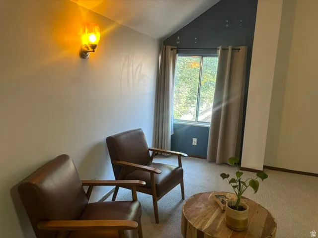 Vaulted ceiling with accent wall, wall-mounted light fixture, window with curtains, and carpeted flooring