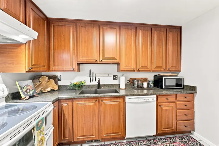 Wood cabinetry with panel detailing, stone-finish countertops, stainless steel sink, and white appliances