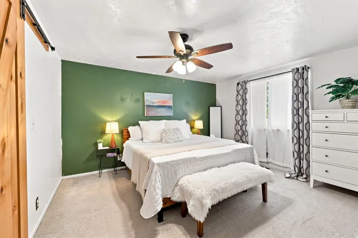 Wood-finish barn door, ceiling fan with integrated lighting, full-height window, and wall-to-wall carpeting