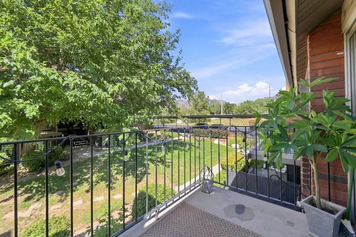 Private balcony with wrought iron railing, concrete flooring, and surrounding mature trees