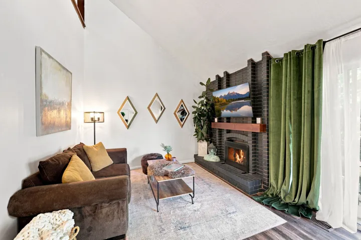 Vaulted ceiling, dark brick fireplace with wood mantel, built-in fireplace insert, wood-finish flooring, and a sliding glass door
