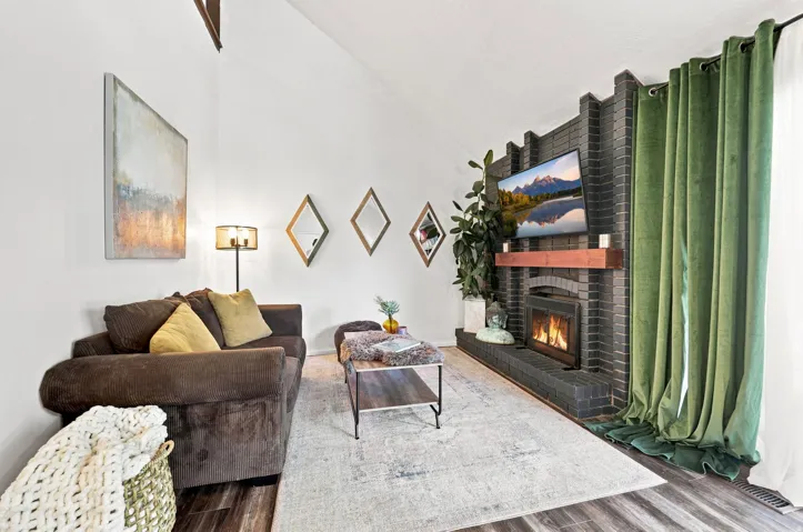 Vaulted ceiling, dark wood-finish flooring, brick-clad fireplace with wood mantel, built-in gas fireplace
