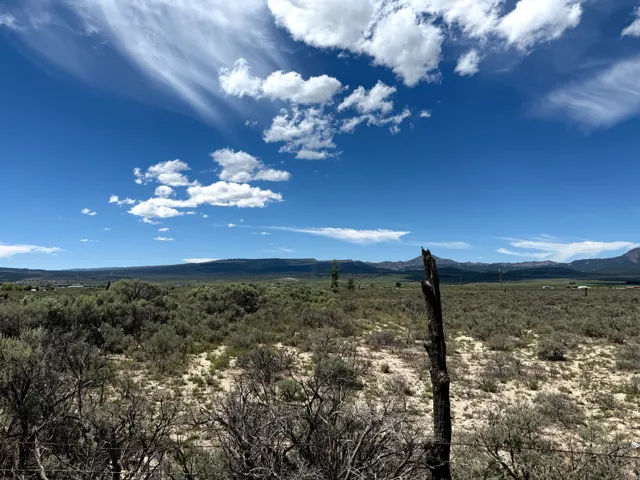 Expansive natural landscape with varied shrubbery, distant mountains, and a clear sky with scattered clouds