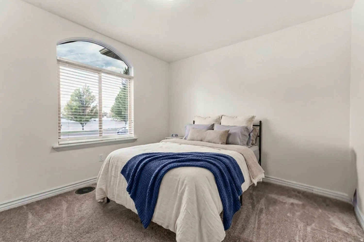Arched window with blinds, white walls, and carpeting