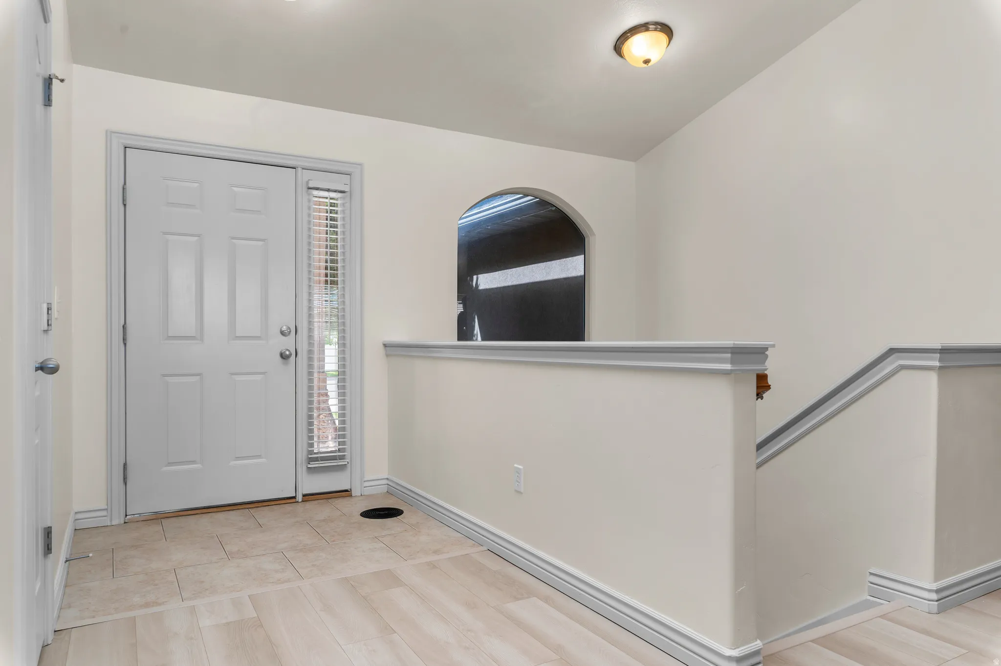 Entryway featuring a panel door with a sidelight, tiled flooring, wood-finish flooring, an arched window opening, and a flush mount light fixture